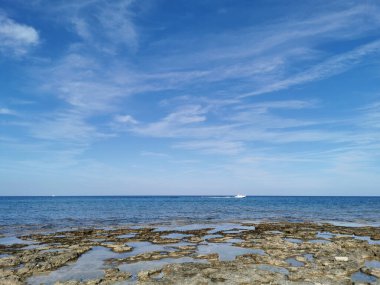 Protaras. Famagusta bölgesi. Kıbrıs. Uzun sert lavlar, Akdeniz kıyıları beyaz bir yatı ve güzel bulutları olan mavi bir gökyüzü olan denizin arka planına karşı..