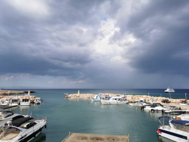 Protaras. Famagusta bölgesi. Kıbrıs. Rıhtım, Akdeniz körfezinde küçük gemileri, yatları ve tekneleri olan liman dramatik bir gökyüzünün arka planına karşı..