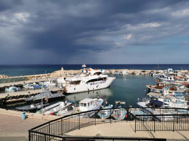 Protaras. Kıbrıs. Rıhtım, Akdeniz körfezinde küçük gemileri, yatları ve tekneleri olan liman dramatik bir gökyüzünün arka planına karşı..