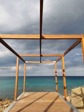 Akdeniz 'in turkuaz sularının üzerinde çarpıcı bir gökyüzüne karşı ahşap çerçeveli bir gözlem güvertesi..