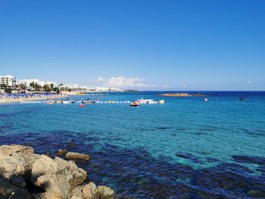 Protaras. Kıbrıs. Akdeniz kıyıları, taş bir tepe, sonunda bir balıkçı, denizde bulutlu mavi bir gökyüzüne karşı beyaz bir zevk yatı.