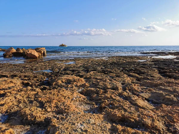 Protaras. Kıbrıs. Akdeniz kıyıları, taş bir tepe, sonunda bir balıkçı, denizde bulutlu mavi bir gökyüzüne karşı beyaz bir zevk yatı.