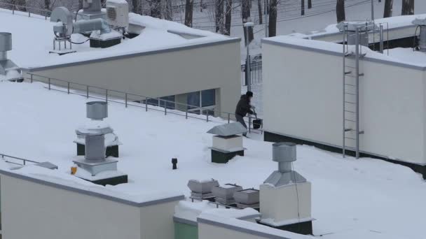 Un homme en hiver nettoie la neige avec une pelle sur le toit d'une maison, un bâtiment et enlève les glaçons — Video