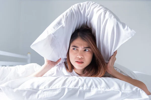 woman uses a pillow to cover her ears from the loud noise on the bed