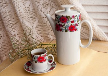 Etrafında beyaz çiçekler olan tahta bir masanın üstünde bir fincan kahve.