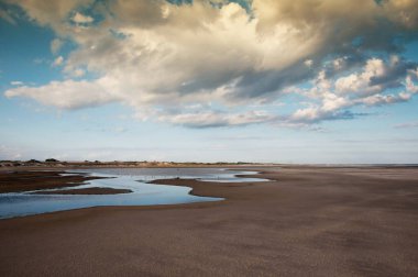 Arkaplanda bulutlar ve gökyüzü ile kumda akan akarsu