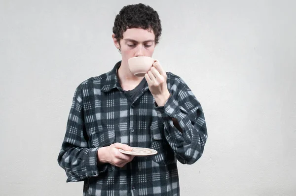 Man in plaid shirt sipping coffee with neutral background