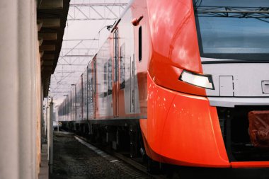 red with a gray high-speed commuter train departing from the railroad station