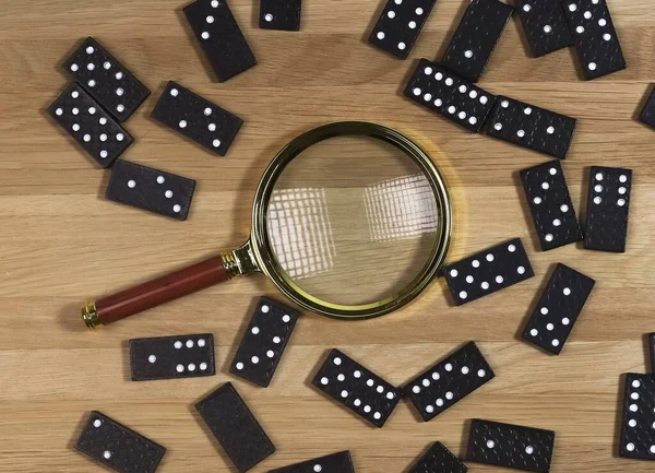 Domino spel bitar utspridda på trä skrivbord med guld förstoringsglas, ovanifrån — Stockfoto