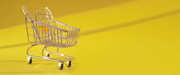 Carrito de compras sobre fondo amarillo brillante con luz de día. Carro de supermercado en banner publicitario con espacio de copia para texto —  Fotos de Stock