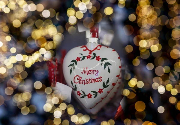 Belarus, Minsk - 18 October 2021 Merry Christmas text on heart-shaped toy with blurred light of Xmas holiday garland — Stock Photo, Image