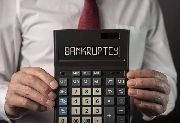 Palavra de bancarrota na calculadora na mão sobre fundo preto — Fotografia de Stock
