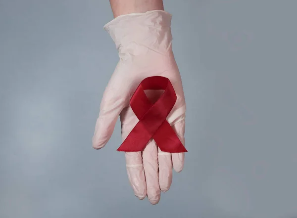 Červená stuha luk jako symbol AIDS a HIV den vědomí, v ruce lékaře detailní — Stock fotografie