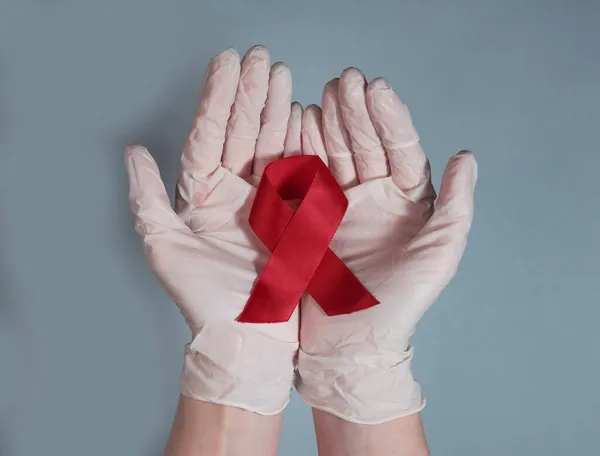 Lazo rojo para la sensibilización sobre el sida y el VIH, en la mano del médico de cerca — Foto de Stock