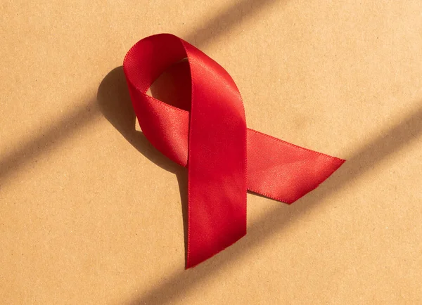 Nastro di raso rosso con anello come simbolo di HIV e AIDS giornata di sensibilizzazione 1 dicembre. Luce del giorno su carta artigianale — Foto Stock