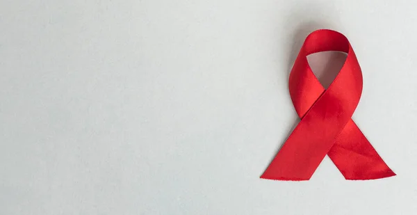 Červená lékařská stuha pro AIDS a HIV den na modrém pozadí s kopírovacím prostorem. Saténová mašle na banneru s místem pro text — Stock fotografie