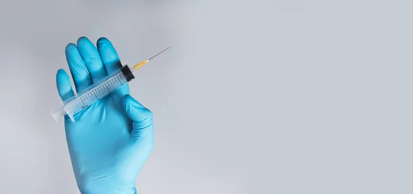 青い灰色の背景に手袋を手に医師の手に鋭い針できれいな注射器。医療広告のコピースペース付きバナー — ストック写真