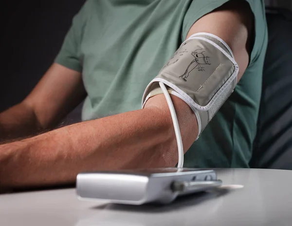 Male hand closeup with cuff of momometer. Blood pressure monitoring and checking by modern tool