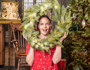 Noel ve yeni yıl arifesinde Noel çelengi içindeki neşeli kadın gülümsüyor ve seviniyor.