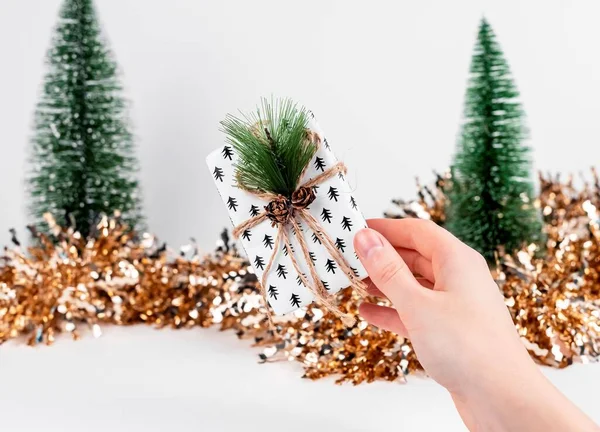 Caja de regalo en las manos y decoración de Navidad con purpurina y abetos —  Fotos de Stock