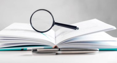 Magnifying lens over open paper book with pages. Concept of academic research