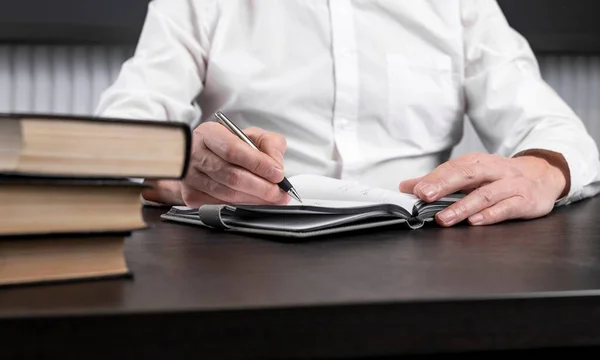 Ofis masasında elinde kitap ve şifrelerle oturan ve günlüğe not alan bir adam. Erkek eli yakın çekim. Planlama veya bilgi analizi kavramı. — Stok fotoğraf