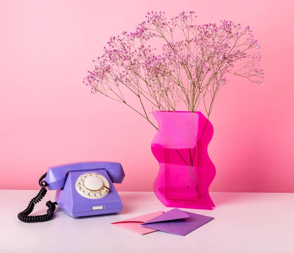 Retro telefoon aan tafel met gedroogde bloemen in vaas en enveloppen. Set van objecten op roze achtergrond. Valentijnsdag concept — Stockfoto