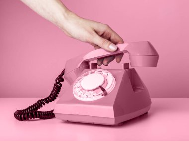 Pembe arka planda retro telefonu tutan ve telefona cevap veren ya da kapatan kadın..