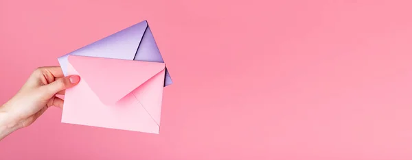 Banner med hand hålla kuvert med alla hjärtans dag hälsning, presentkort, kärleksbrev eller inbjudan på rosa bakgrund. Kopiera utrymme — Stockfoto