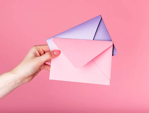 Envelopes mão segurando com dia dos namorados cumprimentos ou certificados de presente em fundo rosa — Fotografia de Stock