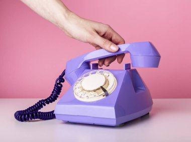 El ele tutuşan eski bir telefon ahizesi, pembe arka planda alıcı. Klasik stil