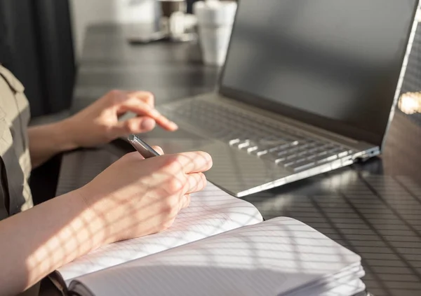 Mulher mãos tomando notas no planejador e trabalhando no laptop no café. Educação online e conceito de trabalho. Fechar. Imagem De Stock