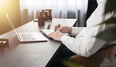 Eller not alıyor, ofis masasında dizüstü bilgisayarla planlama yapıyor.