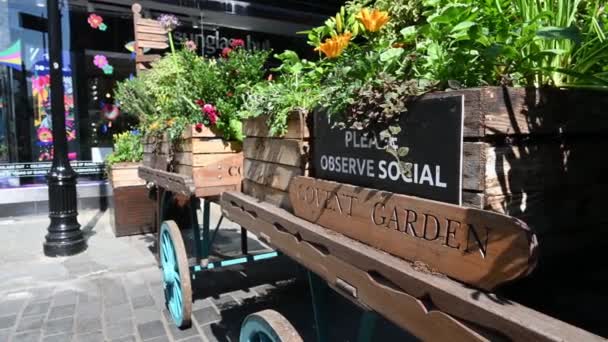 Un letrero de Covent Garden y un letrero de distanciamiento social con personas que pasan caminando usando máscaras faciales — Vídeos de Stock