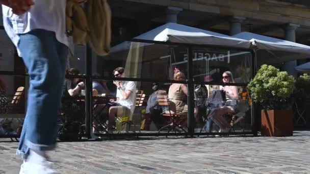 Πλήθη ανθρώπων που περπατούν μπροστά από ανθρώπους που τρώνε έξω σε ένα εστιατόριο στο Covent Garden — Αρχείο Βίντεο