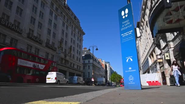 Una vista de ángulo bajo de un cartel COVID junto a la carretera en una calle de Londres con un autobús rojo de Londres de dos pisos en el fondo — Vídeos de Stock