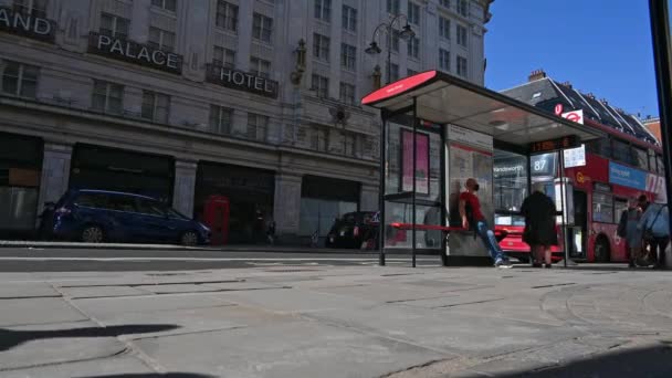 Un autobús se detuvo en una parada de autobús en una calle de Londres con gente caminando en primer plano — Vídeo de stock