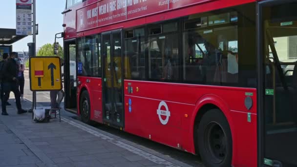 Az arcmaszkot viselő emberek felszállnak egy Red London Double Decker buszra, ami megáll egy buszmegállóban a Waterloo hídon. — Stock videók
