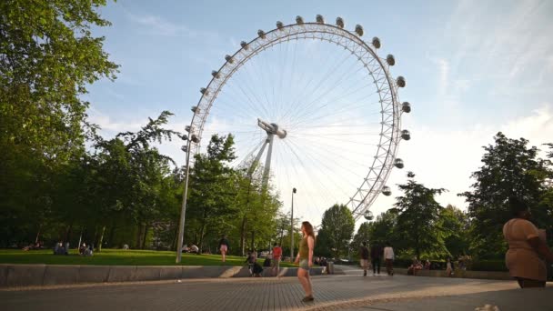 Folk går runt i Jubilee Gardens framför London Eye på en sommarkväll — Stockvideo