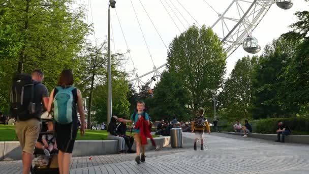 Pessoas caminhando pelos Jardins Jubileu em frente ao London Eye em uma noite de verão — Vídeo de Stock