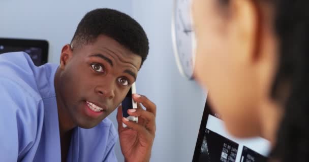 スマート フォンを使用している間女性の同僚に話しているアフリカ系アメリカ人の医者のクローズ アップ — ストック動画