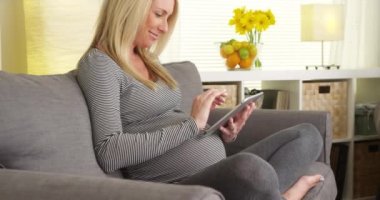 Tablet kullanarak kanepede oturan mutlu hamile kadın