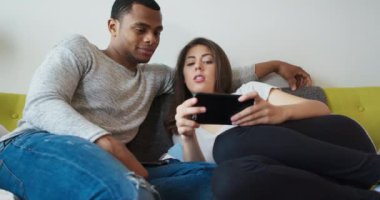 Genç milenyum çifti telefonlarından bir şeye bakarken konuşuyor. Afrika kökenli Amerikalı ve Kafkasyalı sevgili sosyal medyayı kullanarak internette geziniyor. 4k Yavaş çekim el bilgisayarı