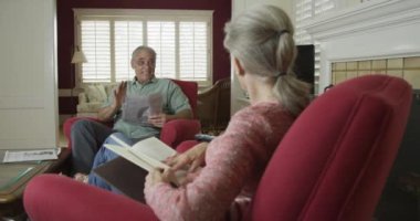 Üst düzey çift içeride oturup kitap okuyor ve konuşuyor.