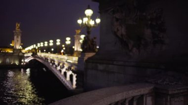 Paris 'teki Seine Nehri' nin karşısındaki Alexandre III köprüsünün romantik gece sahnesi. Paris 'teki ünlü Fransız köprüsündeki bulanık ışık direkleri ve heykeller