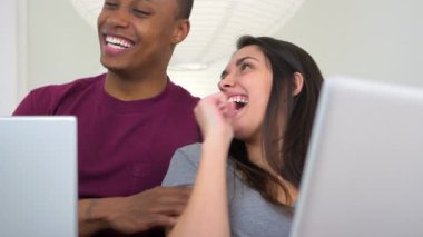 Kanepede dizüstü bilgisayar kullanan Afro-Amerikalı ve Kafkasyalı çift