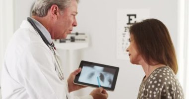 Kıdemli doktor yaşlı hastaya akciğer röntgenlerini açıklıyor.