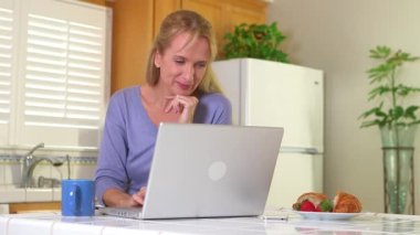 Yetişkin bir kadın bilgisayar kullanırken sabah kahvesini içiyor.