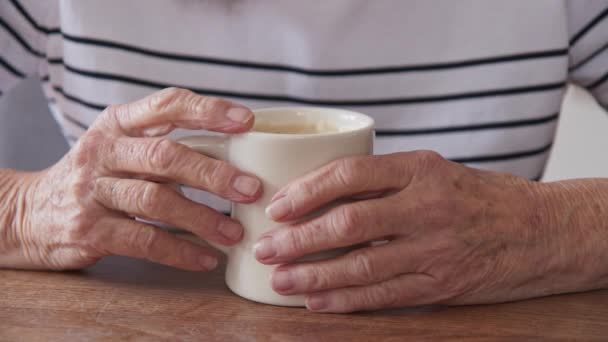 木製のテーブルでコーヒーカップに古い白人女性の手を閉じてください マグカップでモーニングティーを持っているシニア女性 スローモーション4K — ストック動画