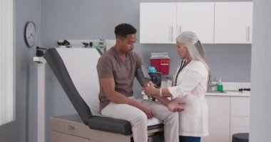 Genç bir erkek hastanın kan basıncını monitör ve steteskopla ölçen olgun bir kadın doktor. Çekici siyah adamın tansiyonu kıdemli beyaz doktor tarafından ölçülüyor.